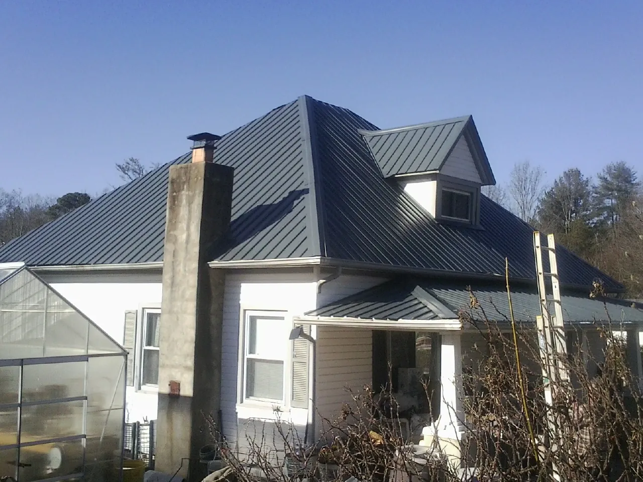 Dark blue standing seam metal roof on a white farmhouse with dormer — Slate & Tile Roof Repair by Roofing Brothers in Commerce Township