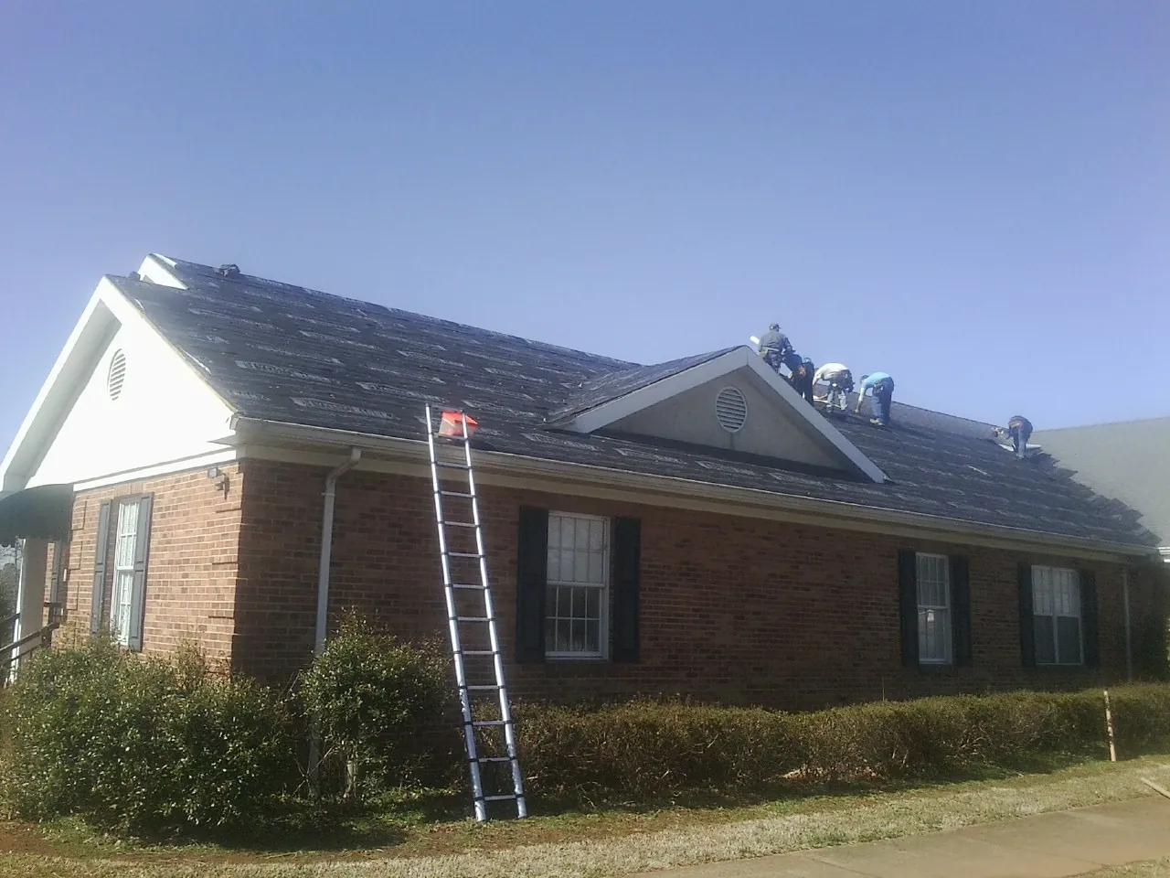 Crew tearing shingles off a brick ranch roof with a ladder set — Metal Roof Repair work by our crew in Commerce Township