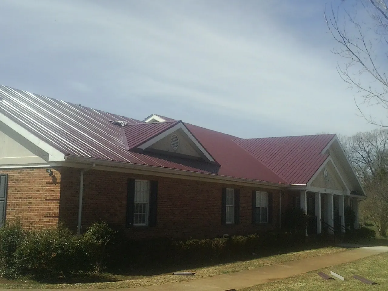 Red metal roof with gabled entries on a long brick building, from a Hail Damage Roof Repair job in Commerce Township