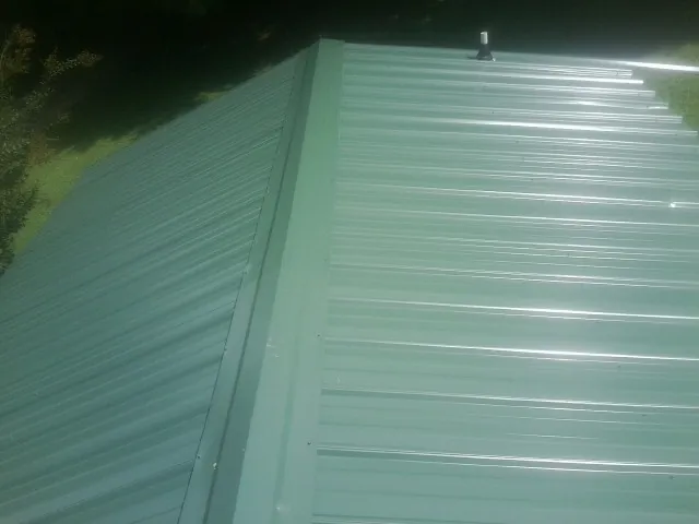 New green metal panels meeting at the ridge of a roof — Flat Roof Repair work by our crew in Commerce Township