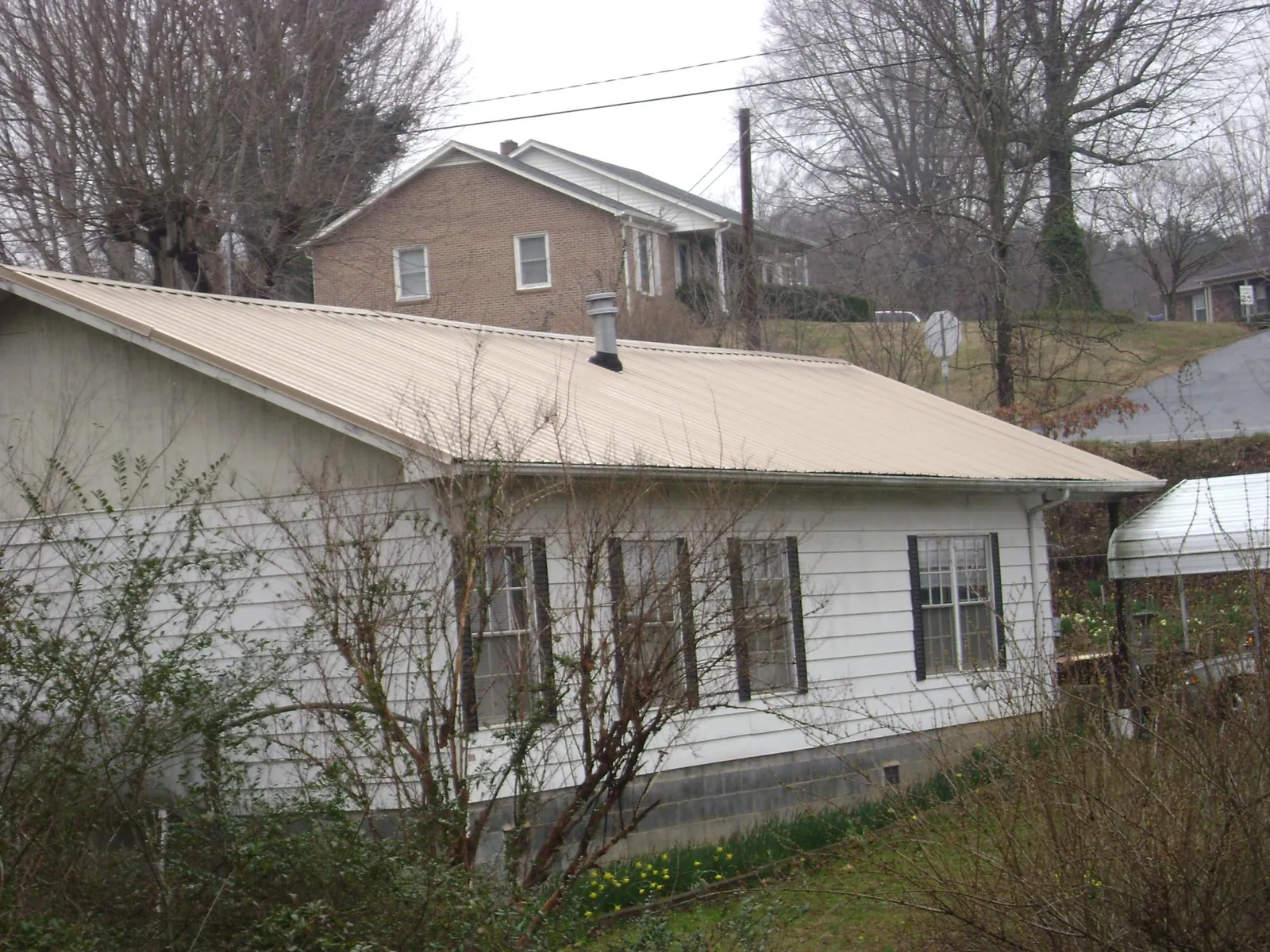 Tan metal roof on a white sided house set into a hillside — Commercial Roofing by Roofing Brothers in Commerce Township