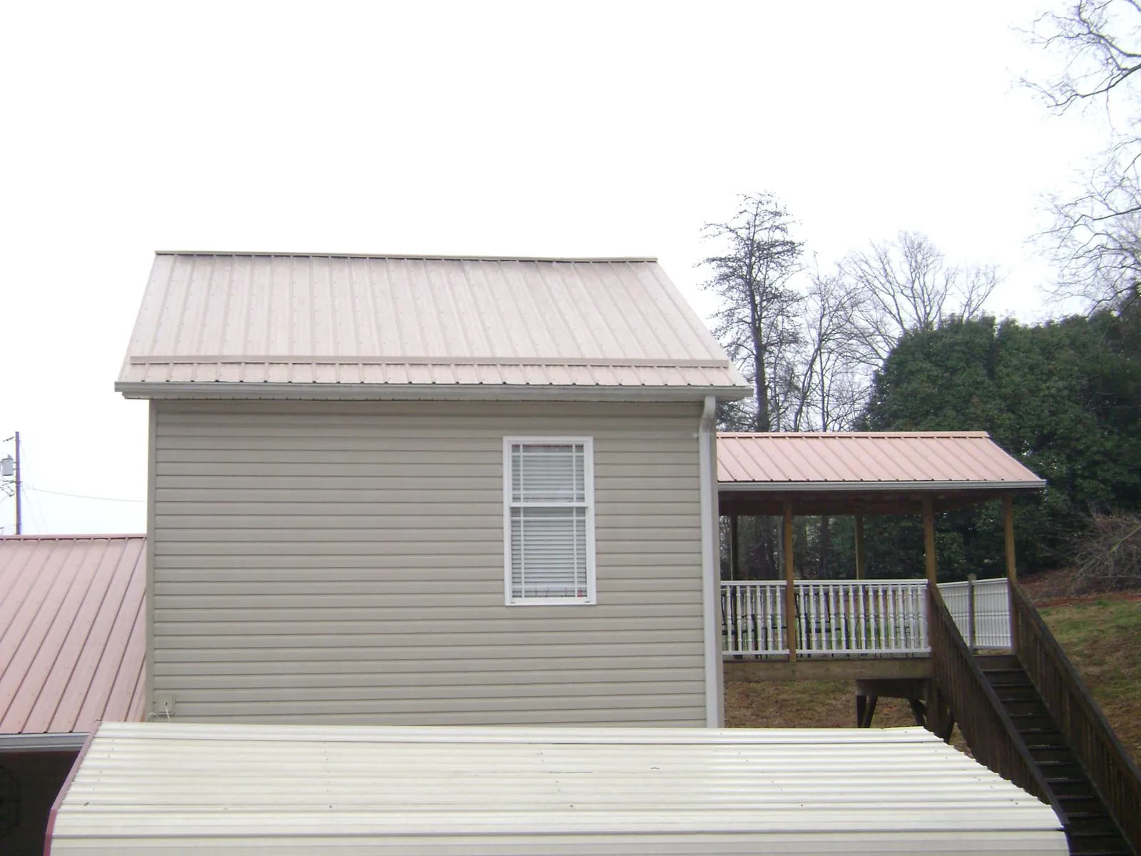 Tan metal roofs on a two story addition and attached porch, from a Roof Replacement job in Commerce Township